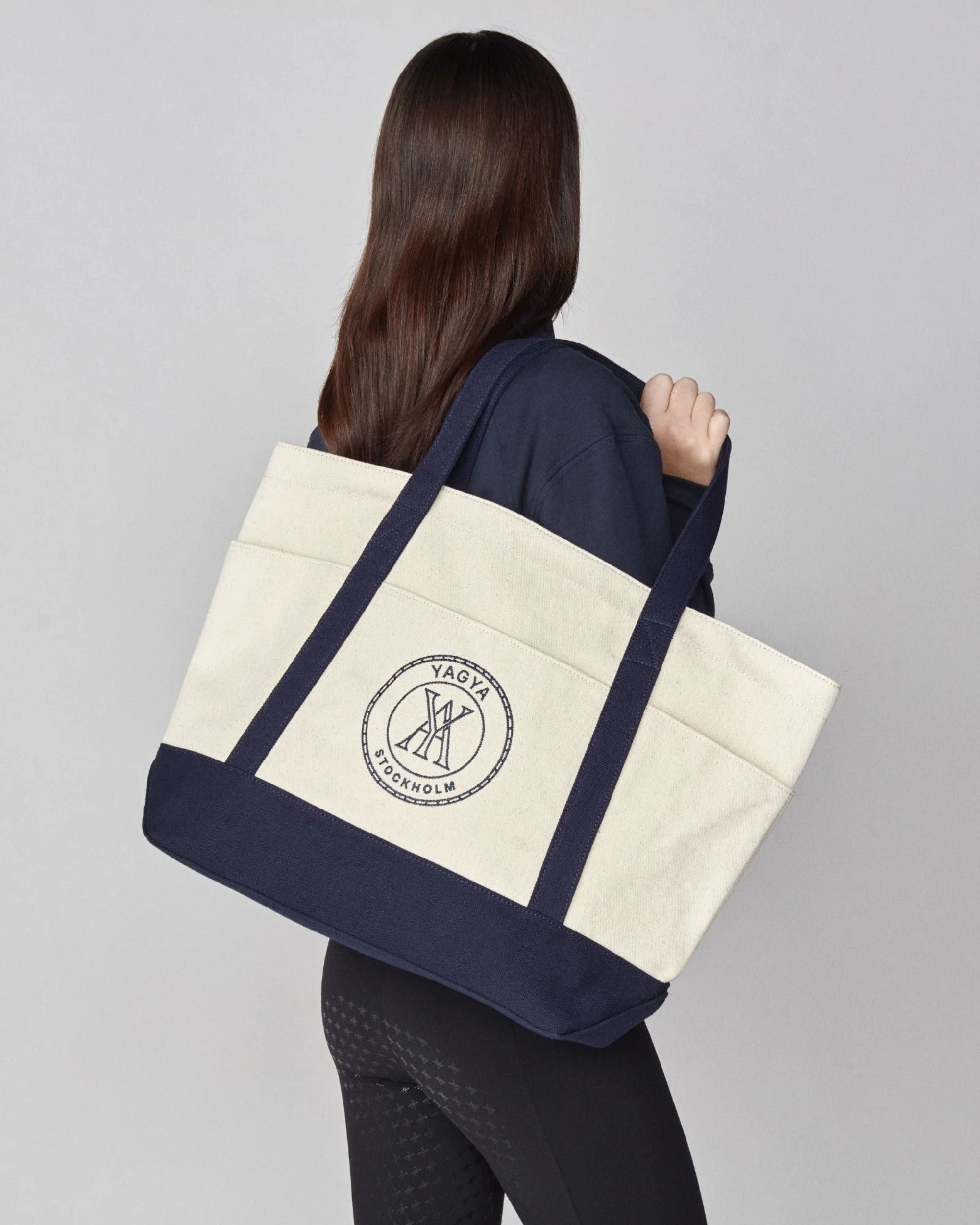 Person holding a navy and beige tote bag with a logo on a gray background