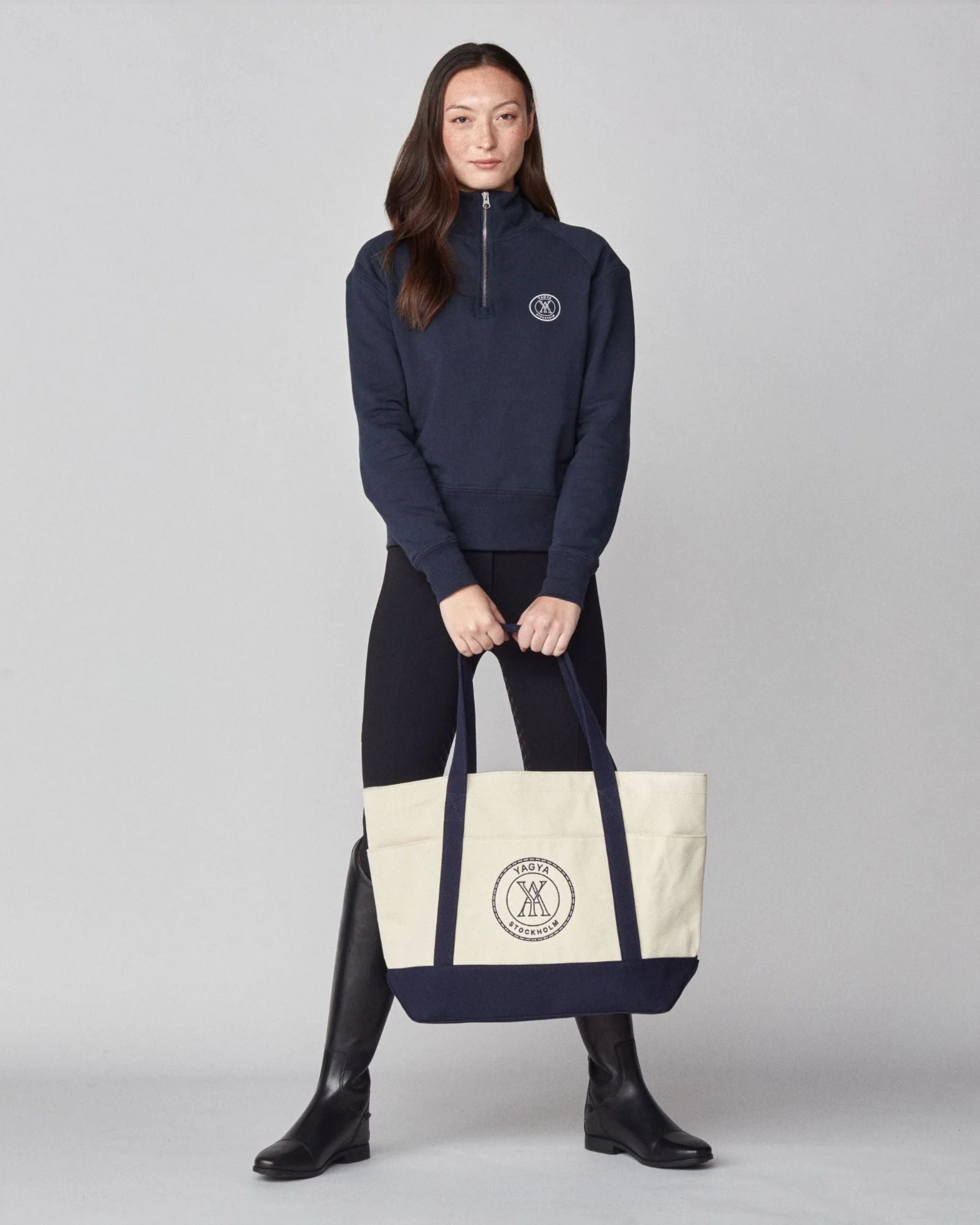 Person wearing a navy blue outfit with a matching tote bag on a gray background