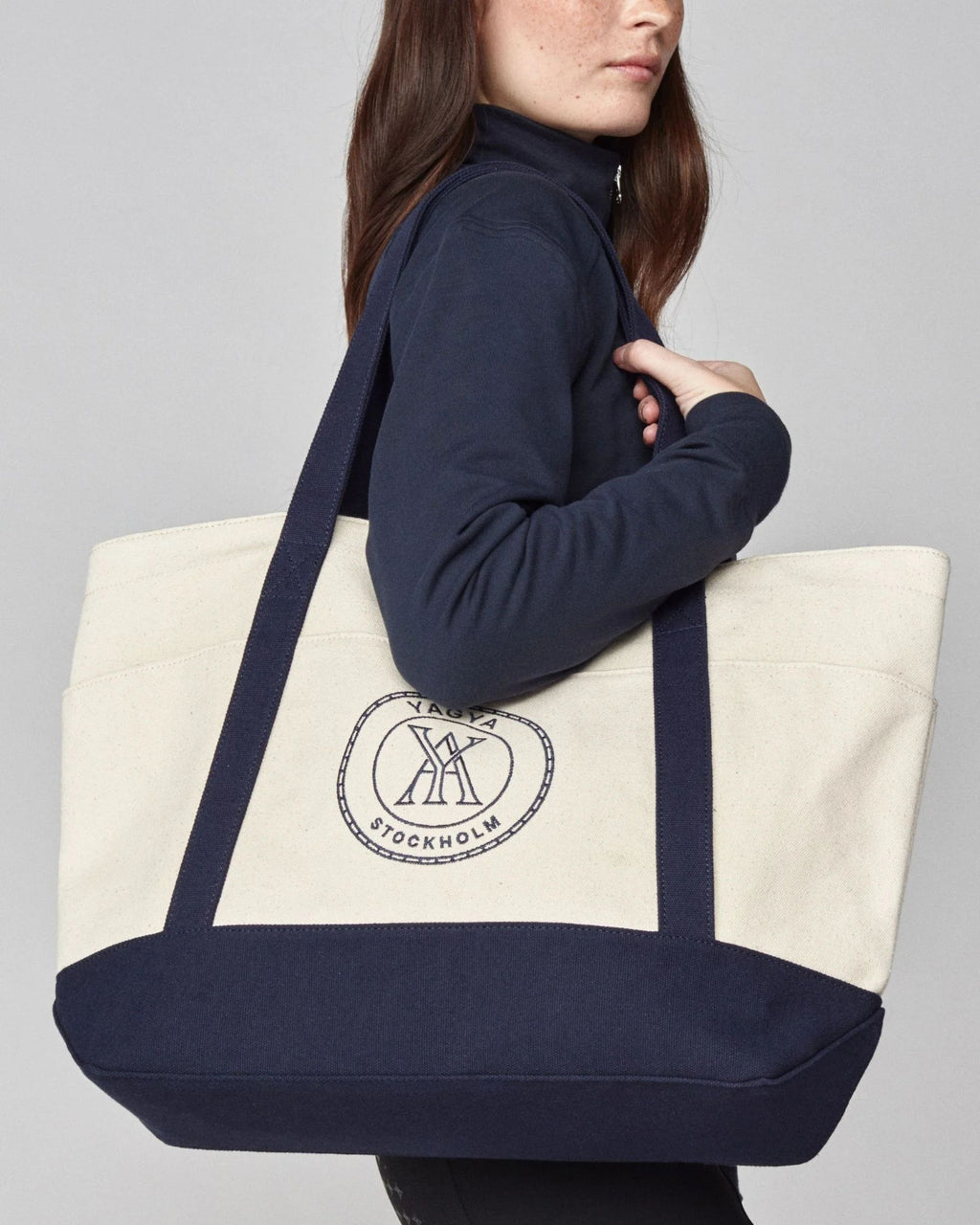 Person holding a navy and white tote bag with a logo on a gray background